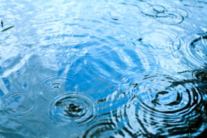 Rain drops rippling in a puddle with blue sky reflection