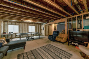 Lounge inside an unfinished basement with wooden beams and wall insulation.